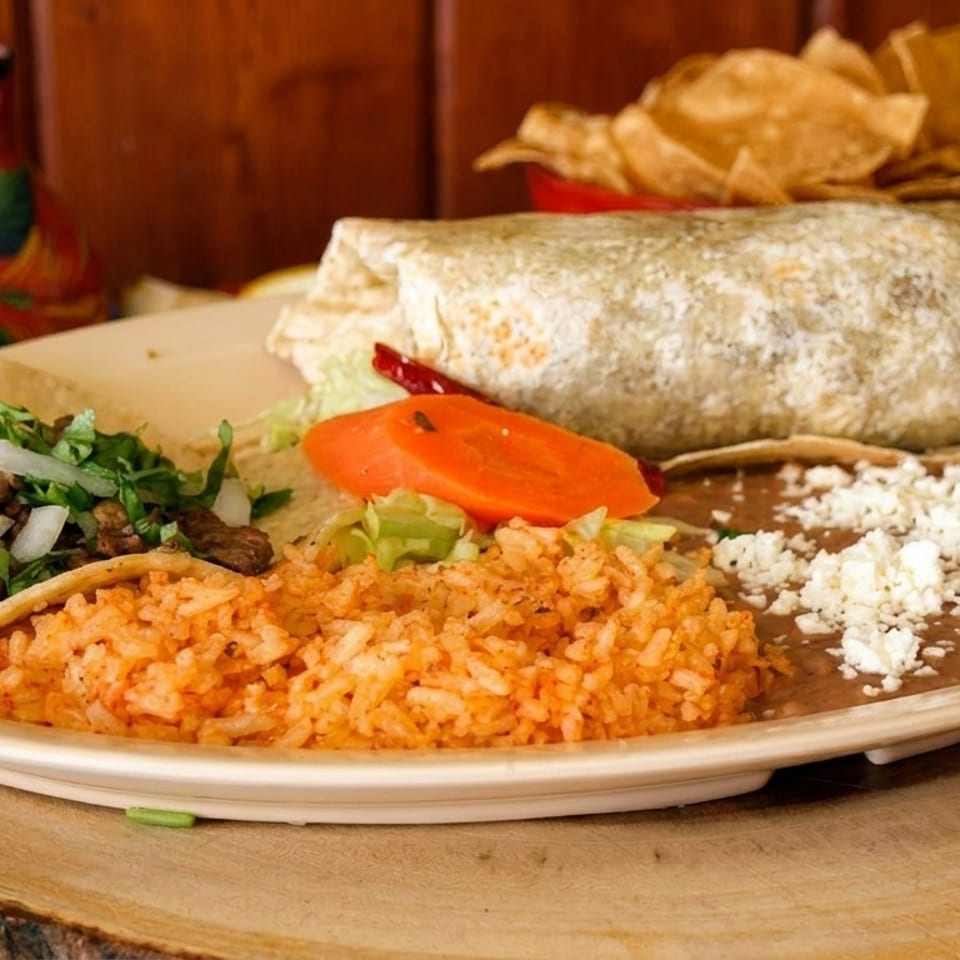 A plate with a burrito, a steak taco, rice, and refried beans topped with cheese.
