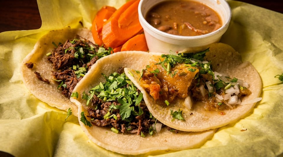 Three street tacos with meat, cilantro, and onions, served with a side of beans and carrots.